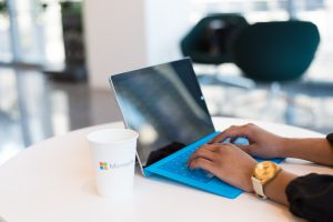 Tablette Microsoft avec tasse en carton et mains